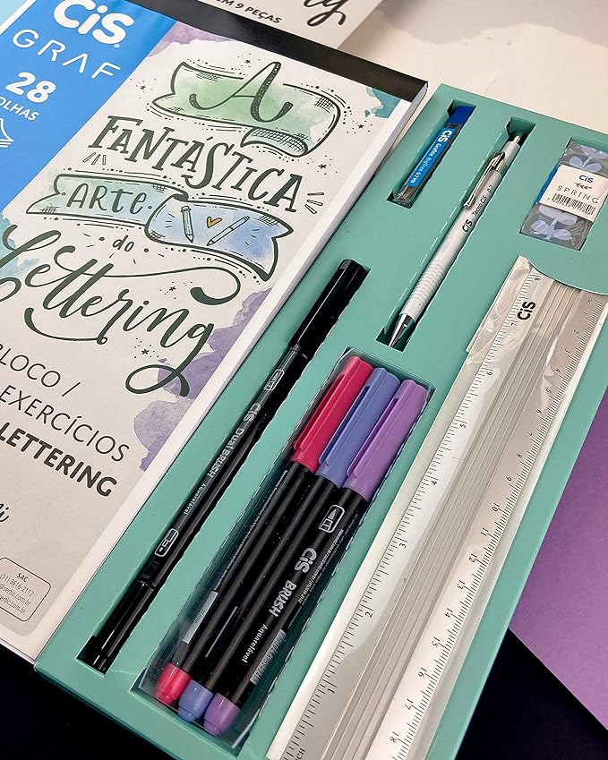 Foco em um kit de Lettering da marca Cis, que contém um caderno de exercícios, uma caneta brush pen de duas pontas, três canetas coloridas, uma lapiseira, grafite, uma borracha e uma régua